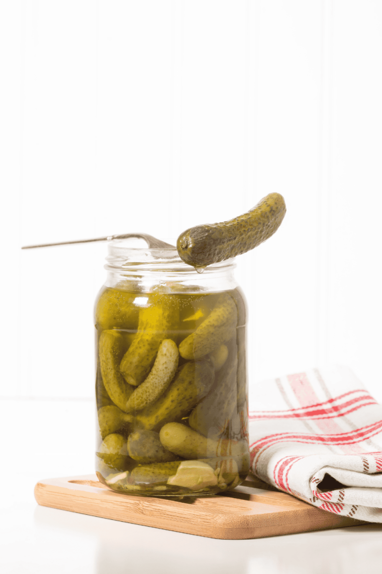 Glass jar of dill pickles on a wooden board with a metal fork lifting one pickle, ready to use for a tangy pickle chicken marinade. This briny base makes the perfect pickle juice chicken marinade for flavorful and juicy dill pickle chicken or a zesty pickle marinade for chicken.