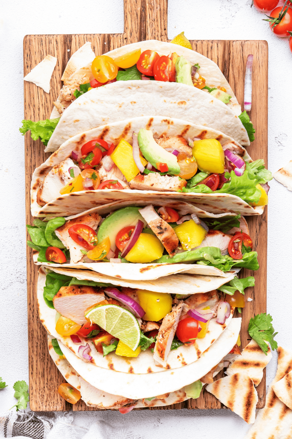 Fresh grilled tacos filled with juicy mango chicken, creamy avocado, and colorful veggies, topped with zesty lime slices and vibrant mango chunks. This bright and tropical dish features tender mango lime chicken with a tangy mango avocado salsa, making it a delicious twist on classic chicken mango recipes for summer meals.