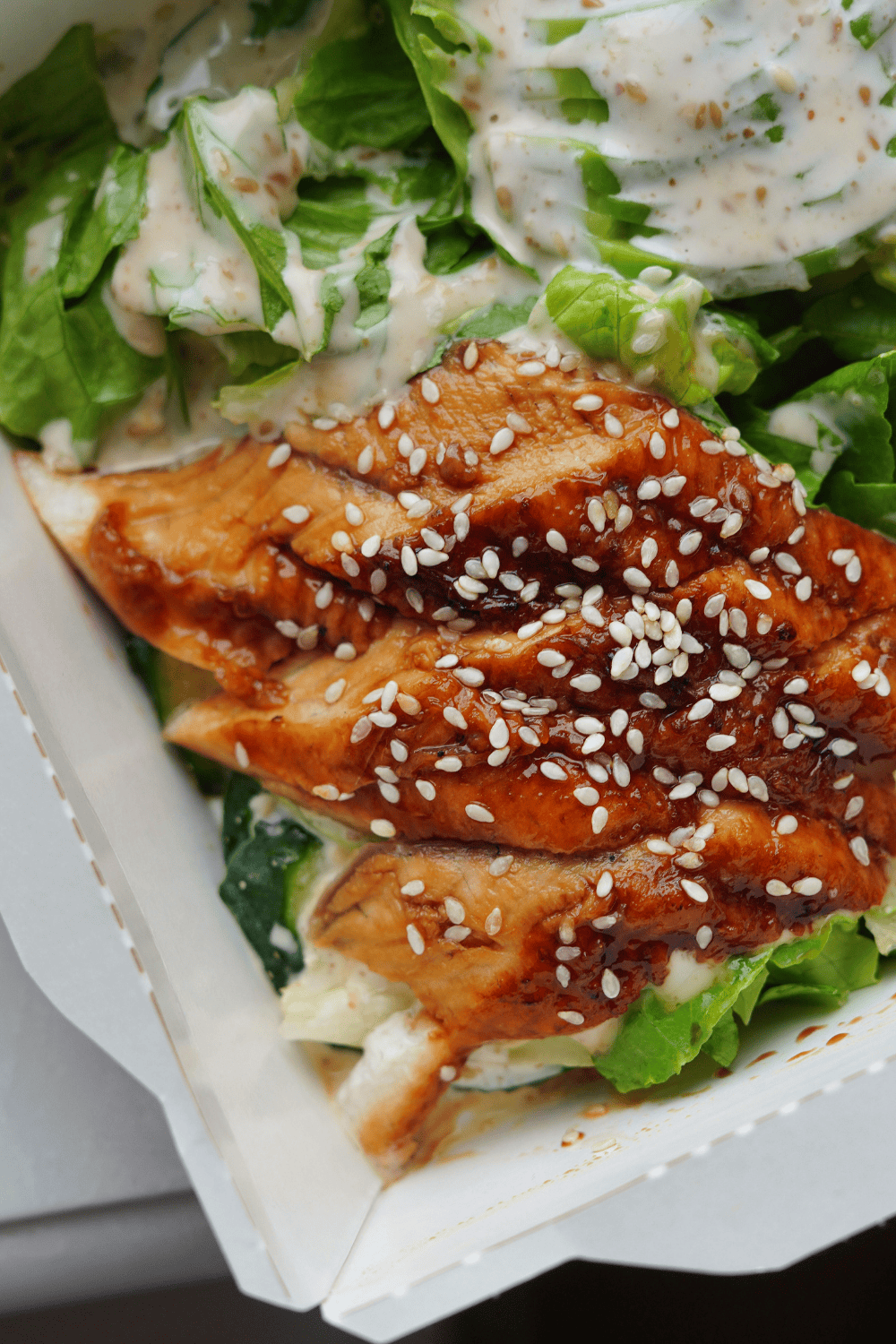 Close-up of juicy sliced sesame chicken glazed in a glossy soy ginger chicken marinade, topped with sesame seeds and served over fresh greens with creamy dressing. This takeout-style sesame chicken recipe easy is packed with flavor from a bold Asian marinade for chicken, perfect for weeknight dinners or meal prep bowls.