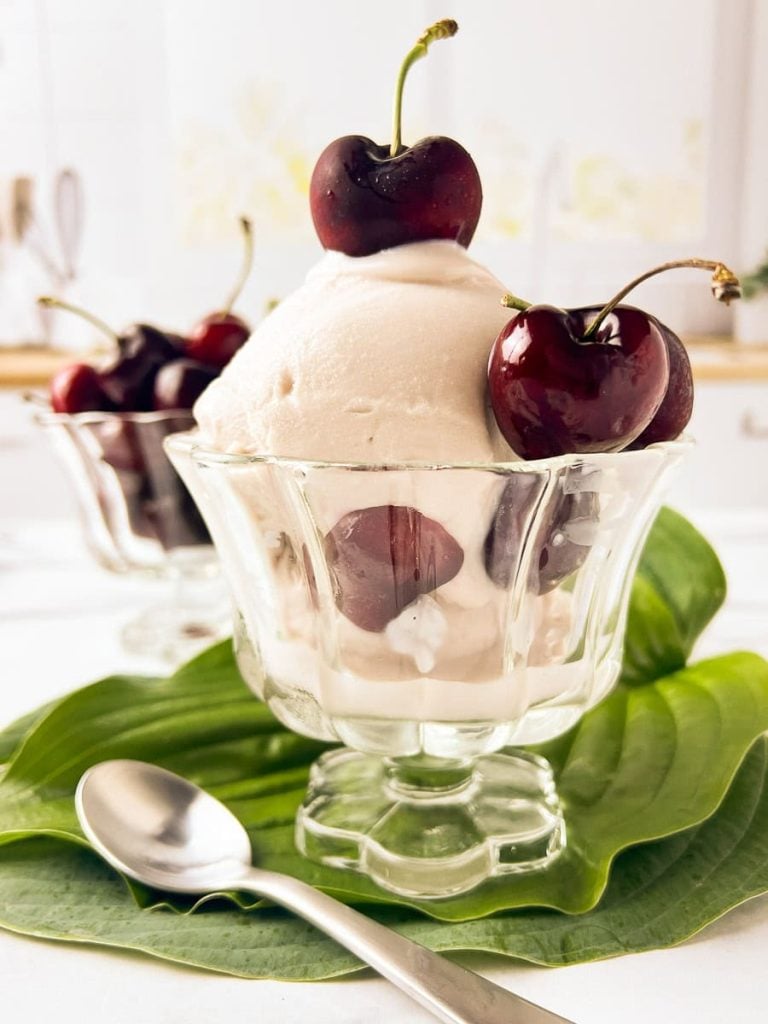 cherry frozen yoguart ninja in a clear footed glass bowl with cherries on top and in the background.