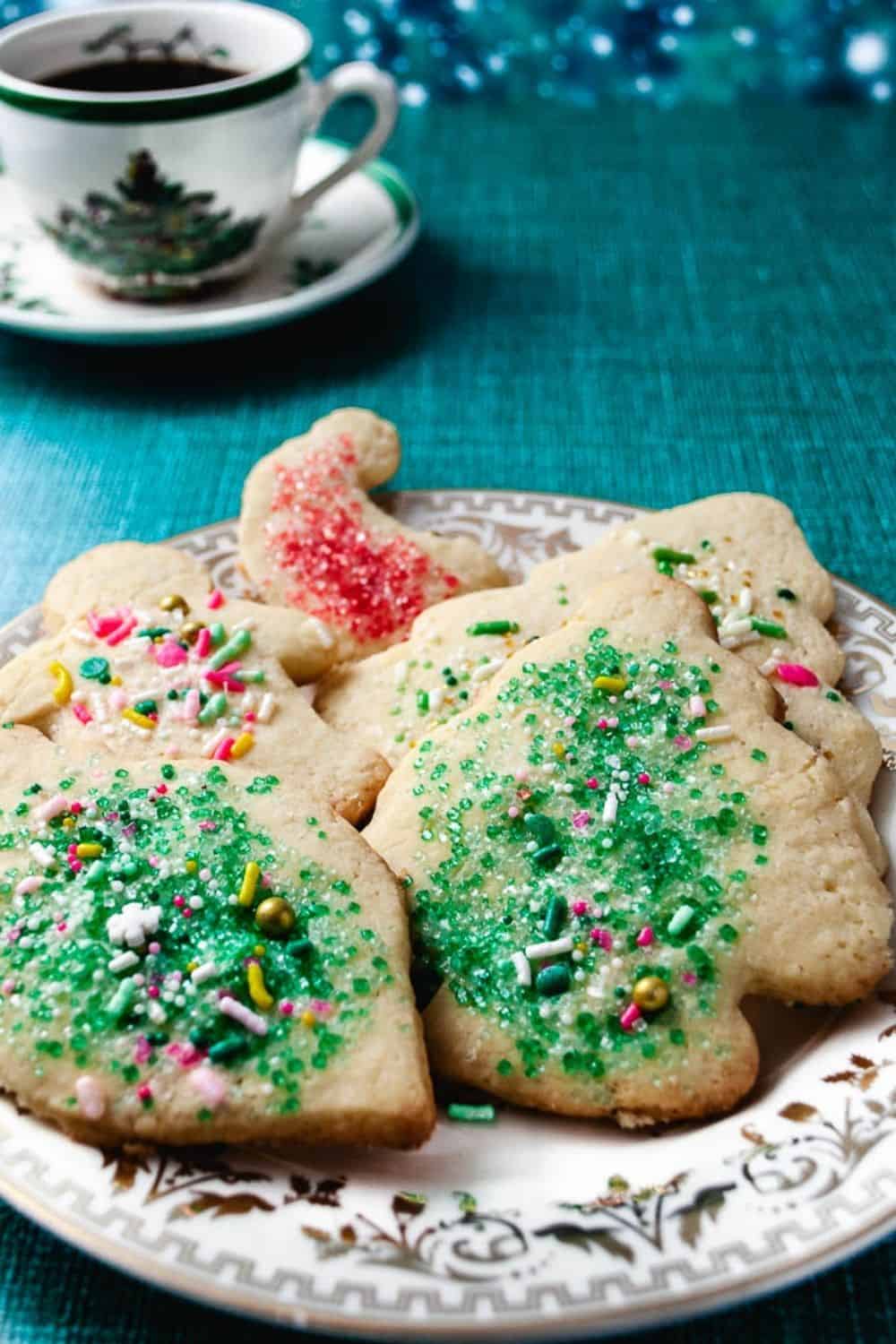 5 cutout sugar cookies on a christmas plate on a teal table with a christmas tea cup.