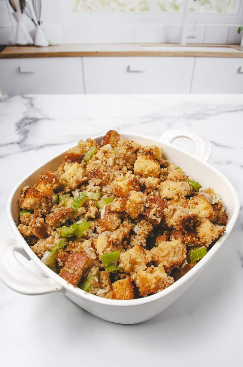 White baking dish filled with easy cornbread stuffing made with homemade cornbread, celery, and onion, set on a marble kitchen counter. A cozy and flavorful Liberty Tree Tavern-inspired recipe perfect for cornbread stuffing recipes, stuffing recipes, and dressing recipes cornbread.