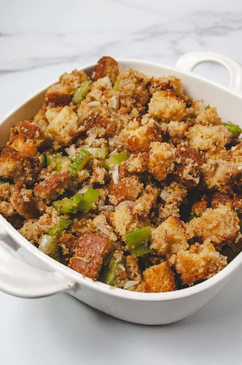 A white baking dish filled with homemade cornbread stuffing, featuring golden cubes of cornbread, chopped celery, and onions. This cozy side dish is a Liberty Tree Tavern copycat and fits perfectly with cornbread stuffing recipes, stuffing recipes, and cornbread easy holiday meals.