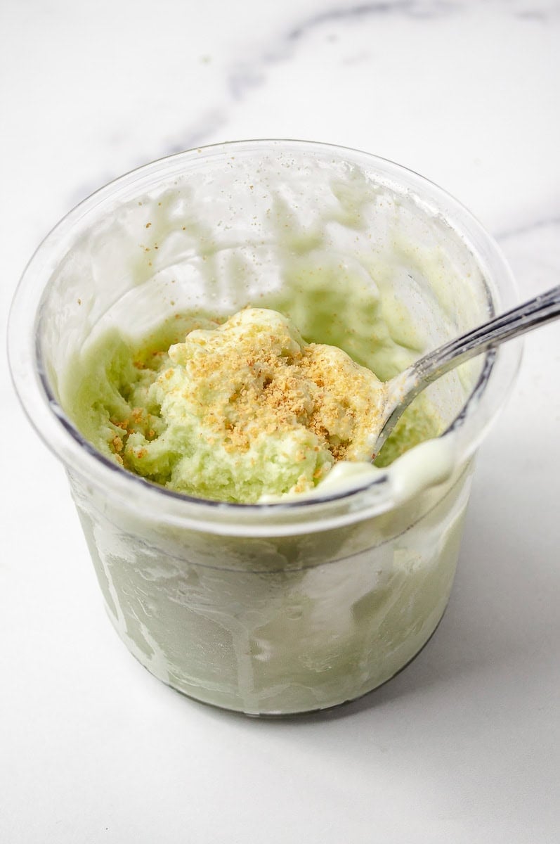 Creamy Pistachio Protein Ice Cream in a Ninja Creami pint, topped with crushed nuts for added texture. Made with sugar-free pudding, Pistachio Pudding, and unsweetened almond milk, this delicious treat is a perfect Sugar Free Ice Cream and part of a satisfying Pistachio Ninja Creami Recipe for those seeking Healthy Ice Cream Recipes.