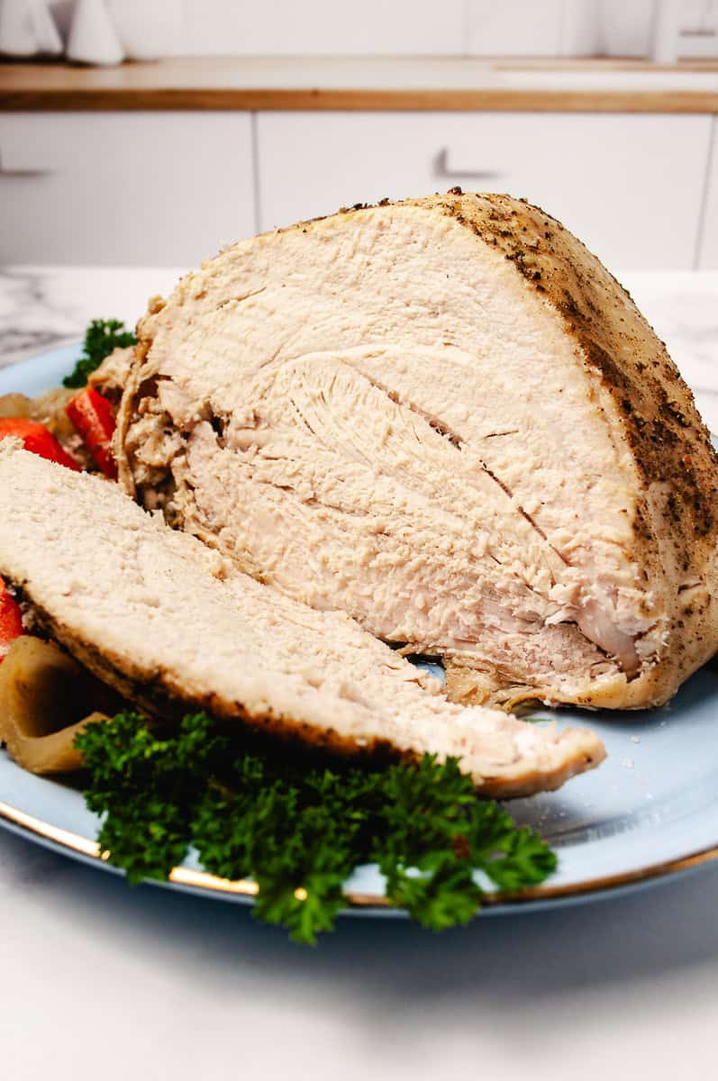 turkey breast cooked in a crockpot with a large slice cut off with parsley an a few carrots.