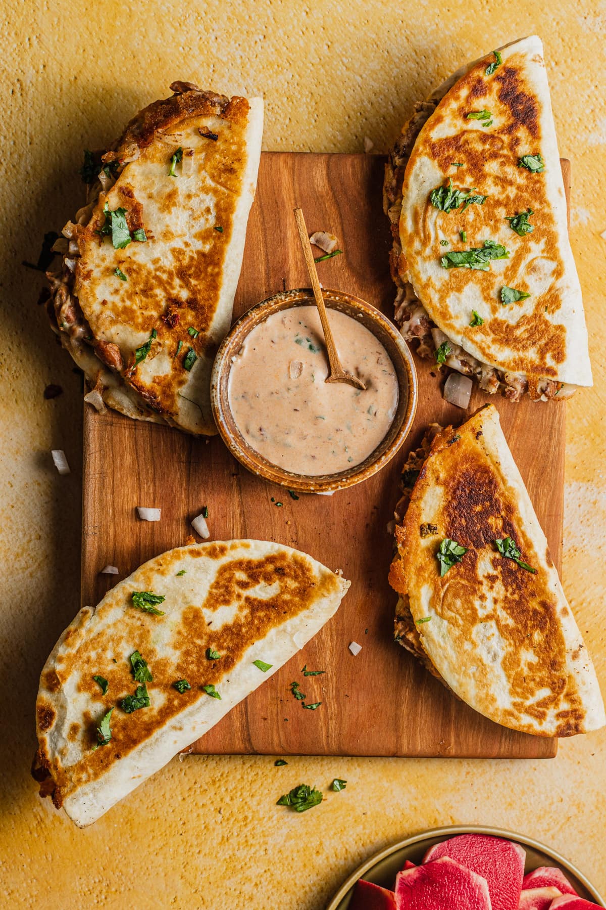 Crispy pan-fried bean and cheese tacos garnished with chopped cilantro, served on a wooden board with a small bowl of creamy chipotle sauce in the center. The tacos are golden brown and filled with melted cheese and refried beans.