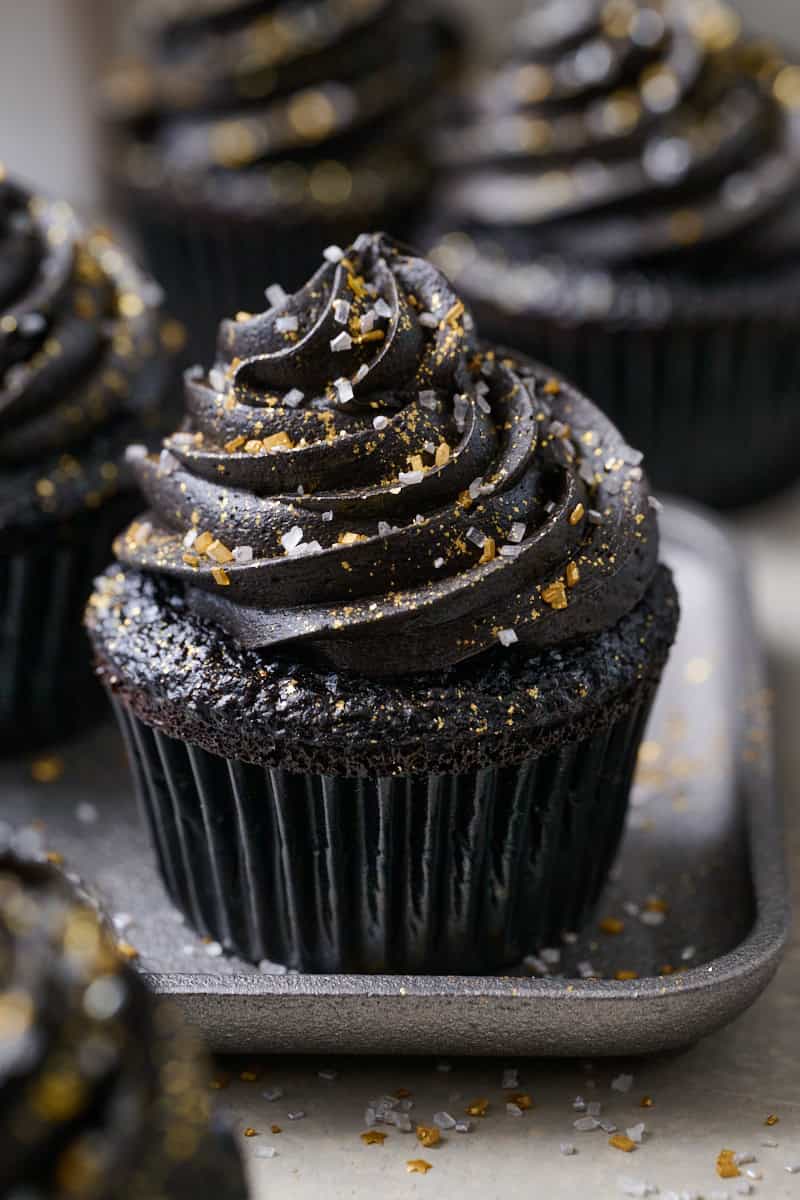 Black velvet cupcake topped with rich black frosting swirled high and sprinkled with gold and silver edible glitter, creating a dramatic and elegant Halloween dessert perfect for parties.