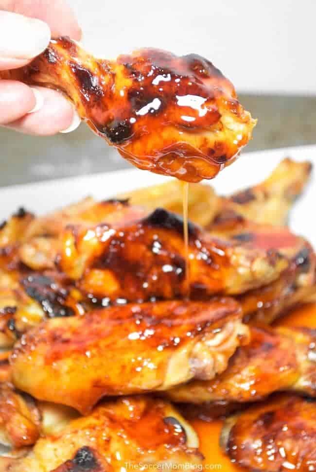 Honey chipotle wings on a white plate with a woman's hand holding up one wing dripping honey on the plate.