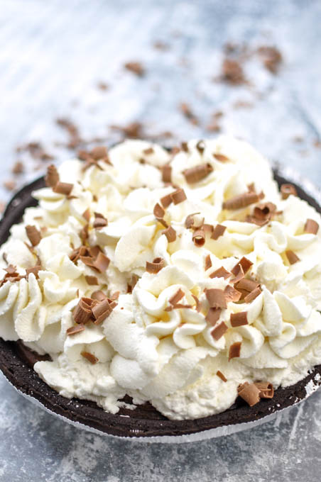 no bake chocolate pudding pie with whipped topping on top and chocolate shavings in a chocolate cookie crust on white counter.