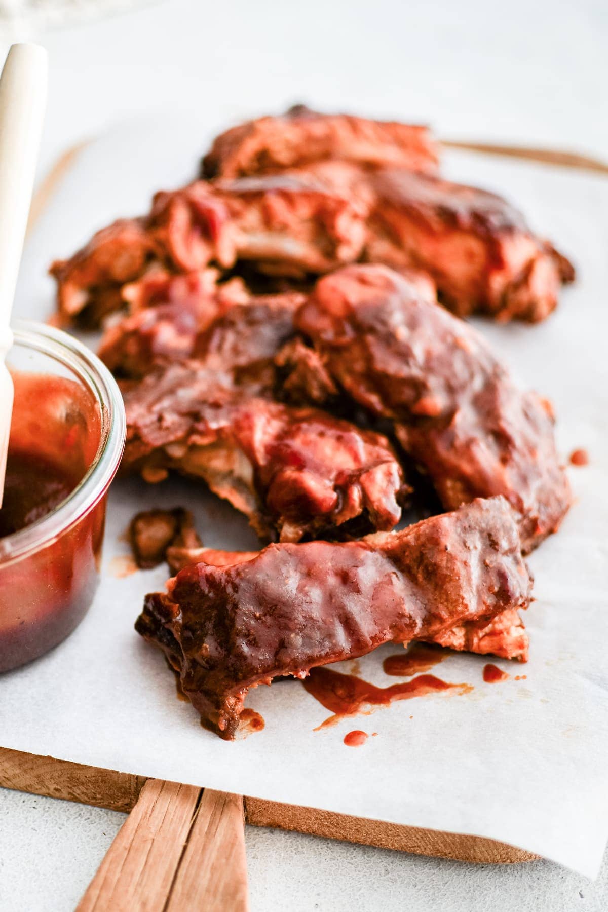 Tender slow cooker baby back ribs coated in sticky barbecue sauce, served on parchment paper with a small jar of extra sauce and a basting brush on the side. The ribs are juicy and fall-apart ready, perfect for game day or party serving.