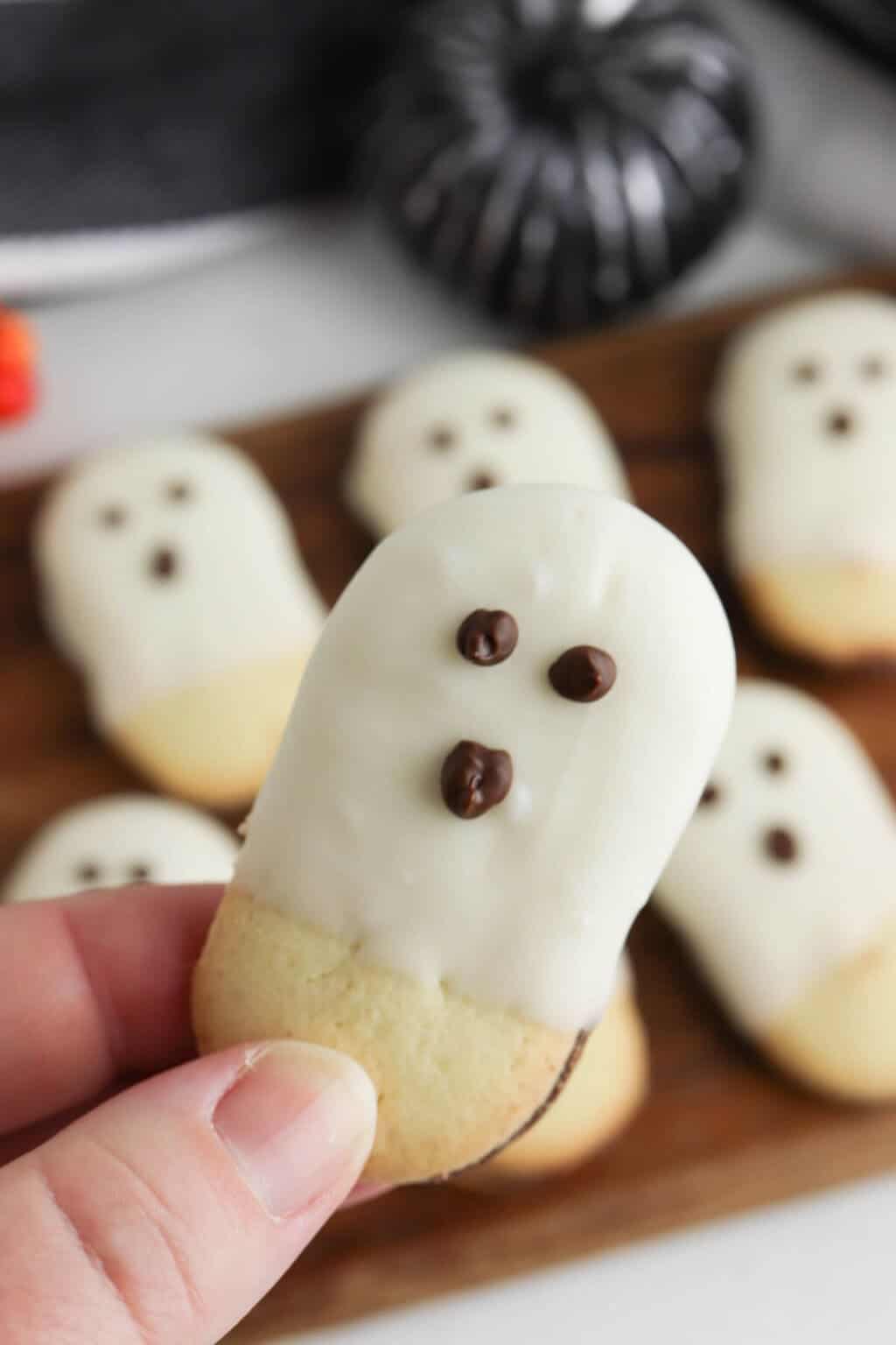 Milano cookies dipped in white chocolate and decorated with chocolate faces to look like little ghosts, arranged on a tray for a fun and easy no-bake Halloween dessert.
