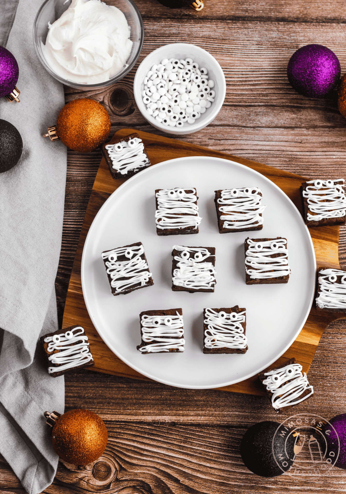 Fudgy brownie squares decorated with white icing drizzled like mummy bandages and candy eyes, arranged on a plate for a fun and spooky Halloween dessert.