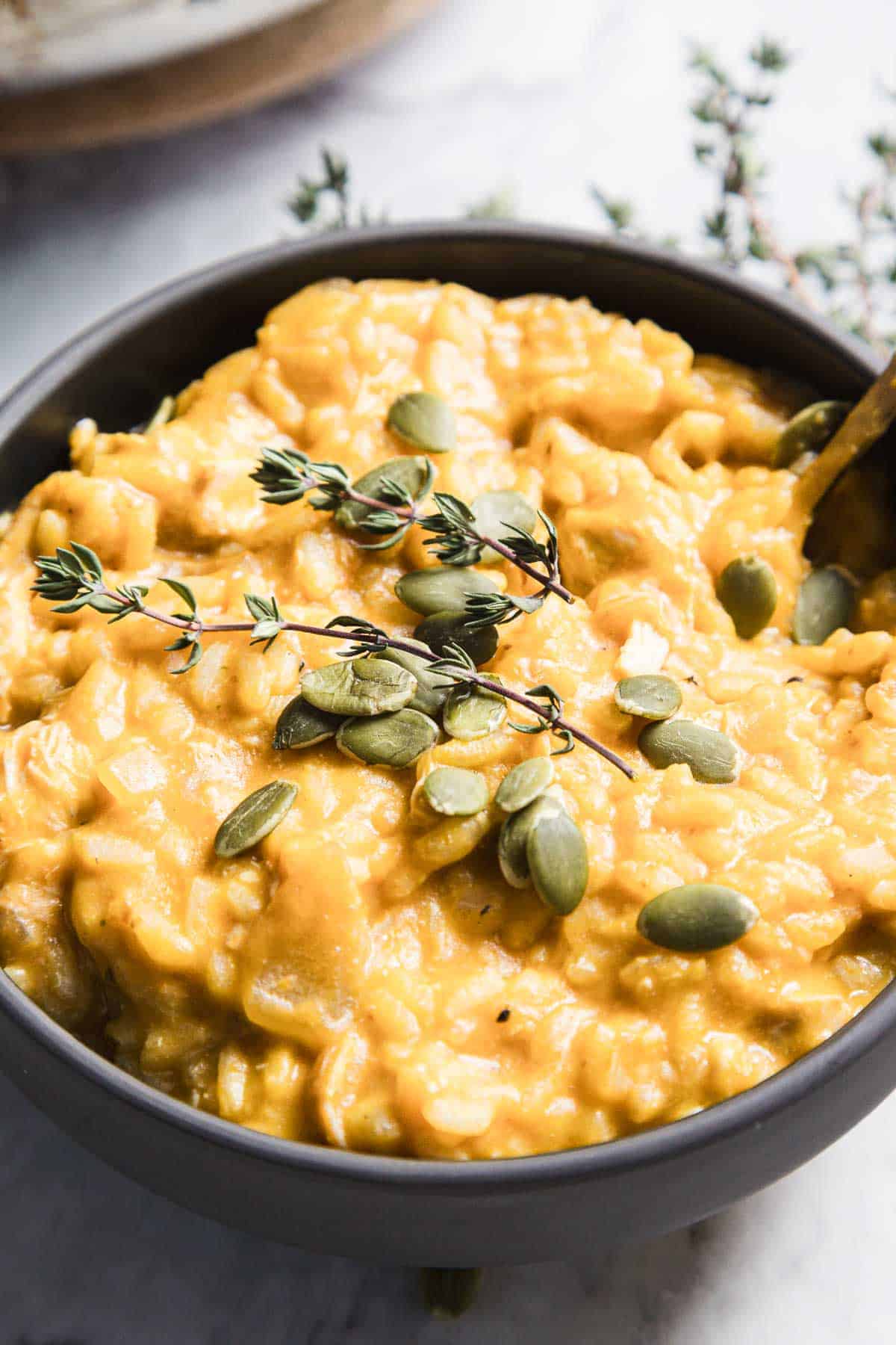 Creamy chicken pumpkin risotto in a bowl topped with fresh thyme and pumpkin seeds, a cozy fall dinner recipe full of savory pumpkin flavors.