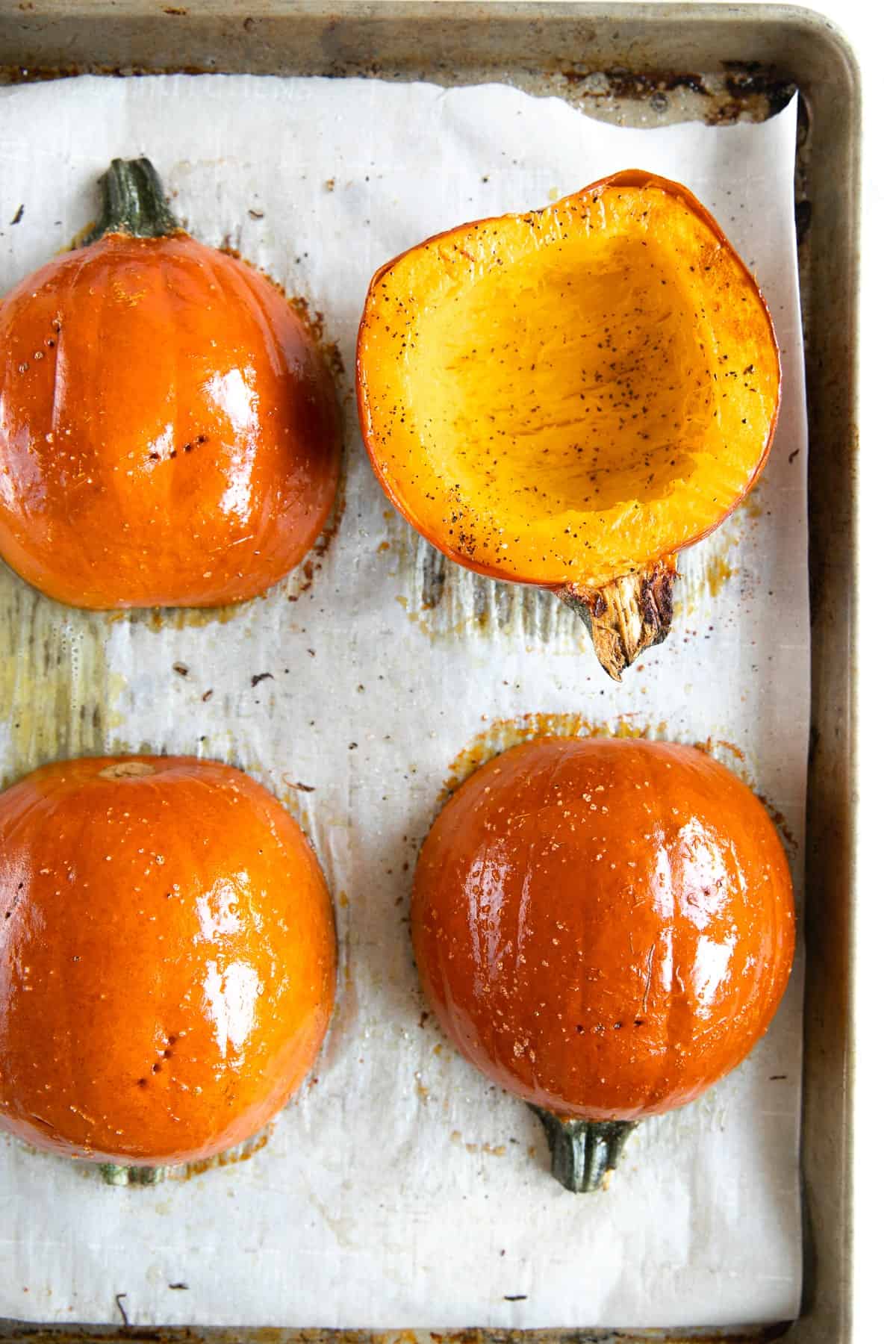 Halved sugar pumpkins roasted on a baking sheet, showing golden flesh and seasoned skin for a simple step-by-step guide on how to cook pumpkin.