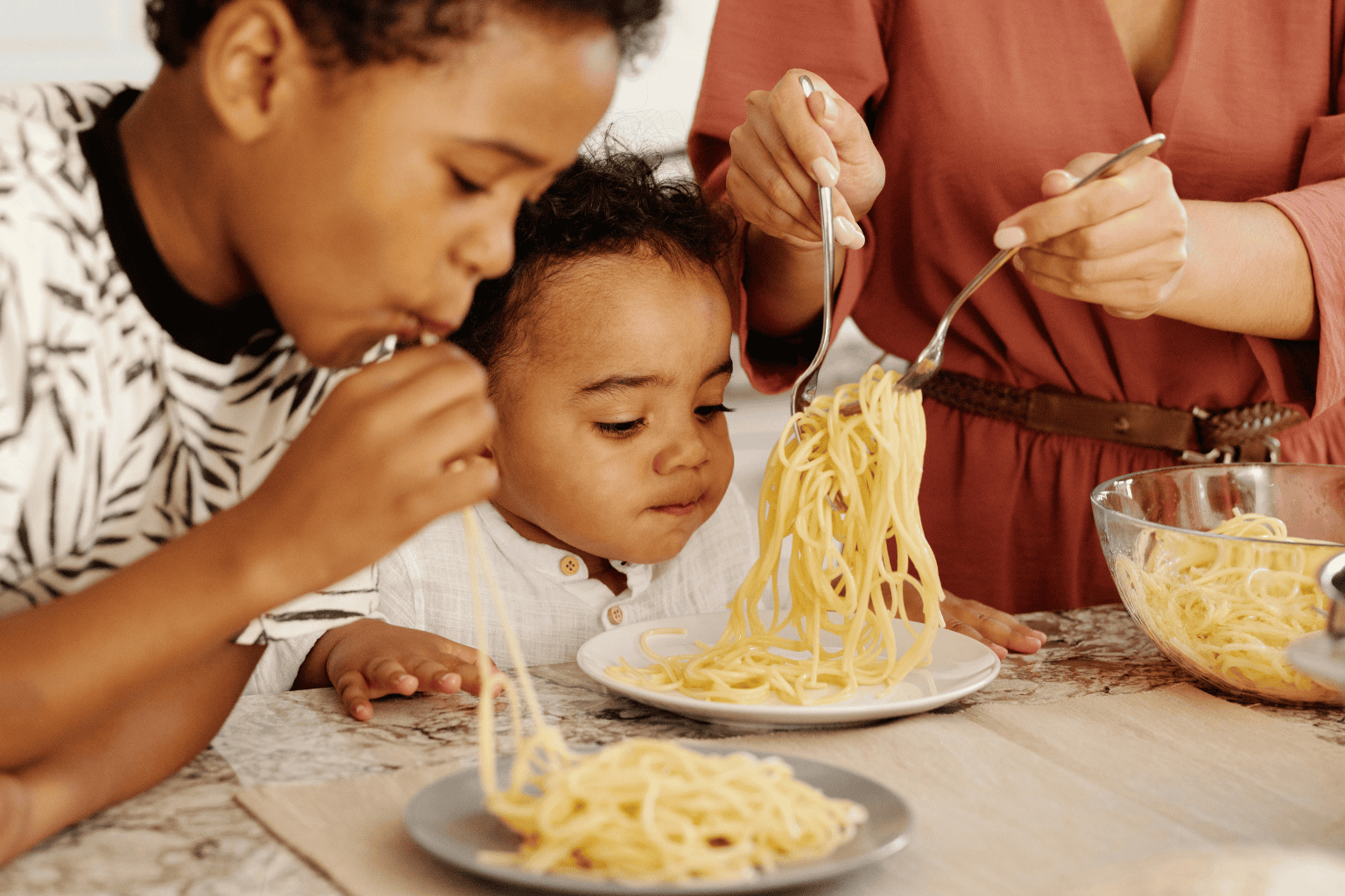 Parent serving cooked spaghetti to two kids at the tableβfamily pasta dish; helpful for a pasta calculator on how much pasta to cook.