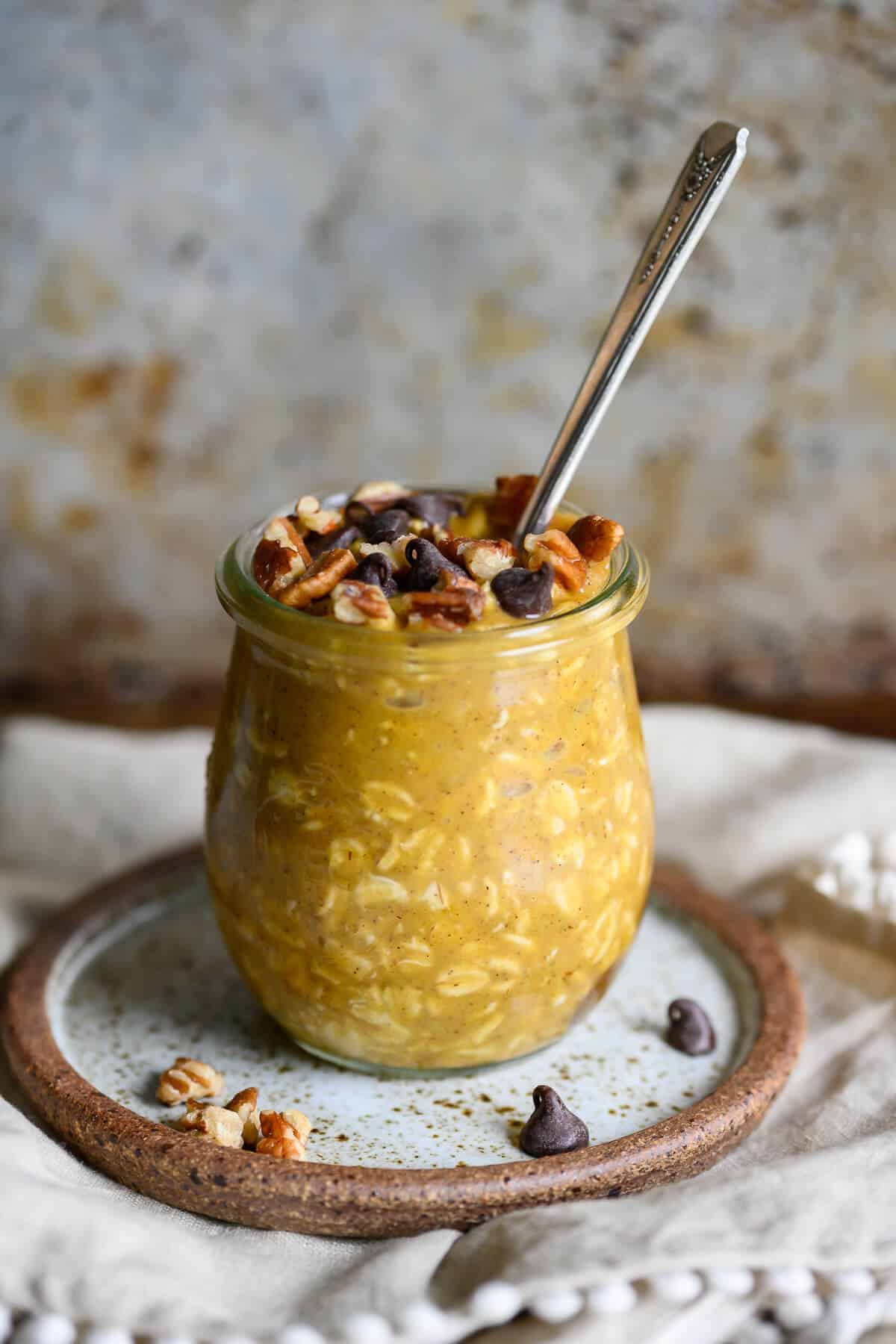 Jar of pumpkin chocolate chip overnight oats topped with pecans and chocolate chips, served with a spoon for an easy fall breakfast.