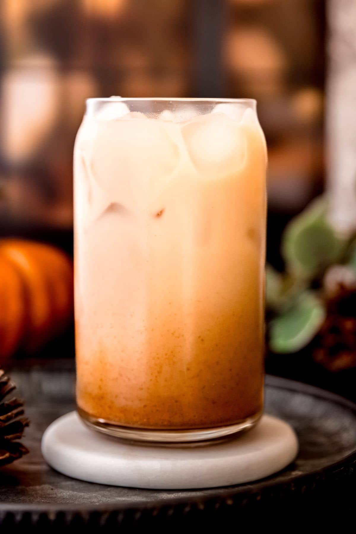 Glass of iced pumpkin spice shaken espresso with creamy layers, served on a dark tray with fall decorations in the background.