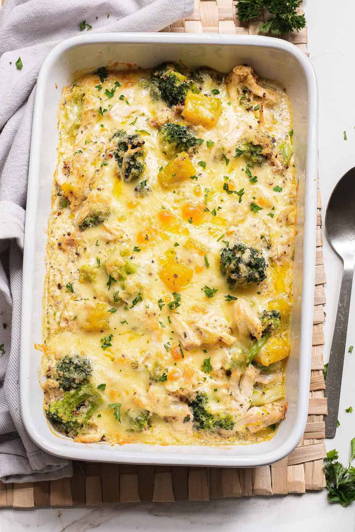 Baked quinoa chicken casserole with broccoli and pumpkin in a white dish, topped with melted cheese and fresh herbs for a cozy fall dinner recipe.