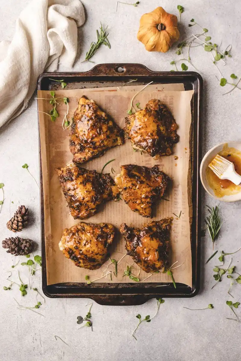 Baked chicken thighs brushed with pumpkin glaze on a sheet pan, garnished with herbs for a savory fall dinner recipe.