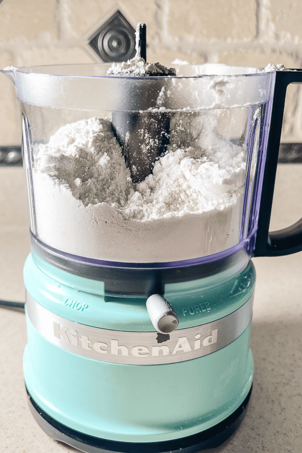 A mini KitchenAid food processor filled with flour, sugar, and salt, ready to mix the dry ingredients for an easy homemade pie crust. The setup shows the first step in making a flaky pie crust recipe for a buttery, perfect pie crust.