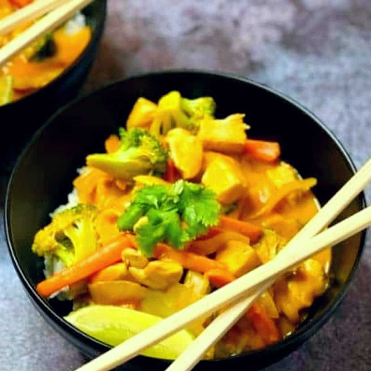 Pumpkin curry with broccoli, carrots, and chicken served over rice in a black bowl with chopsticks and fresh cilantro garnish.