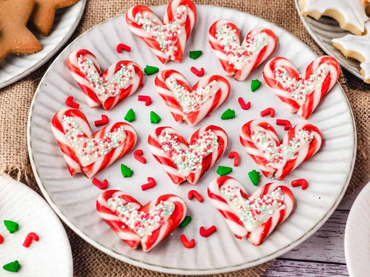 Candy cane hearts filled with white chocolate and festive sprinkles, arranged on a holiday plate with red and green decorations.