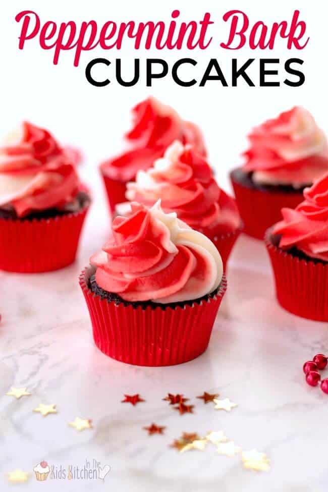 Chocolate peppermint bark cupcakes in red liners, topped with swirled red and white frosting, surrounded by holiday confetti stars on a marble surface.
