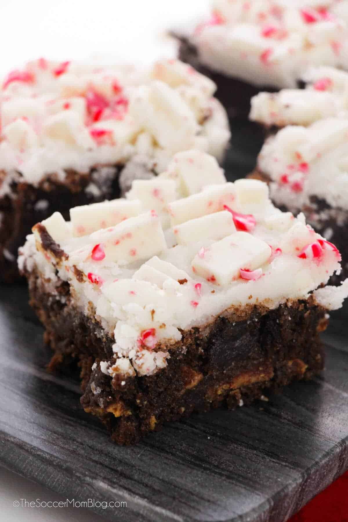 Fudgy peppermint bark brownies topped with white chocolate chunks and crushed peppermint, displayed on a dark serving board for a festive holiday dessert.