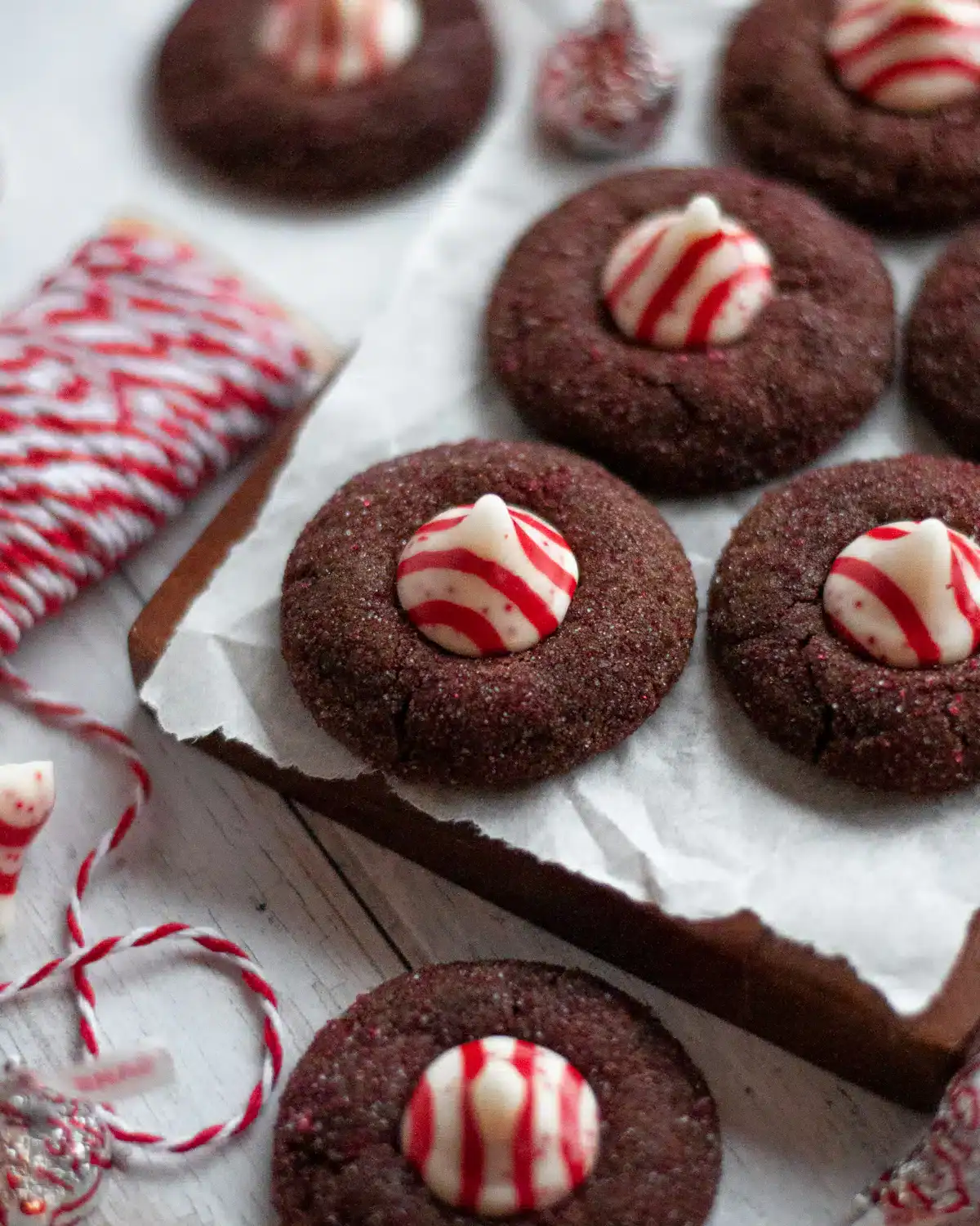 Chocolate peppermint kiss cookies topped with striped Hershey’s peppermint kisses, arranged on parchment paper with red and white twine and holiday decor.