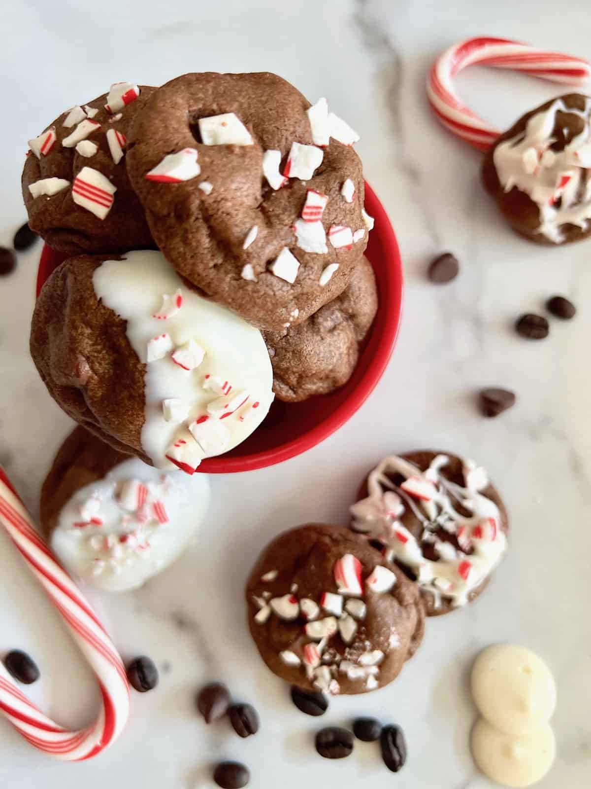Peppermint mocha cookies topped with crushed candy canes and drizzled white chocolate, arranged on a marble surface with candy canes, chocolate chips, and coffee beans.