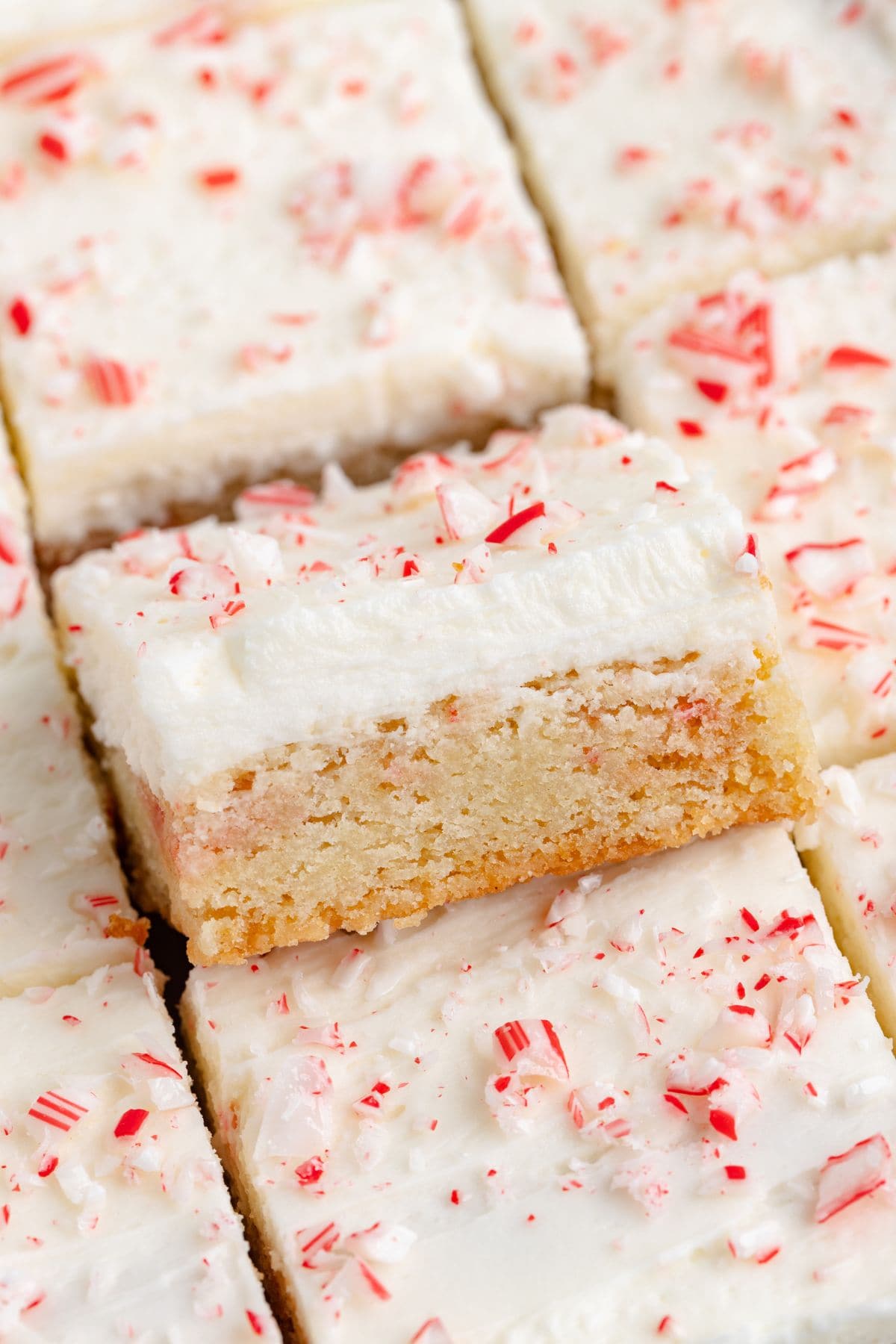 Peppermint sugar cookie bars topped with thick white peppermint frosting and crushed candy canes, cut into squares and stacked for serving.