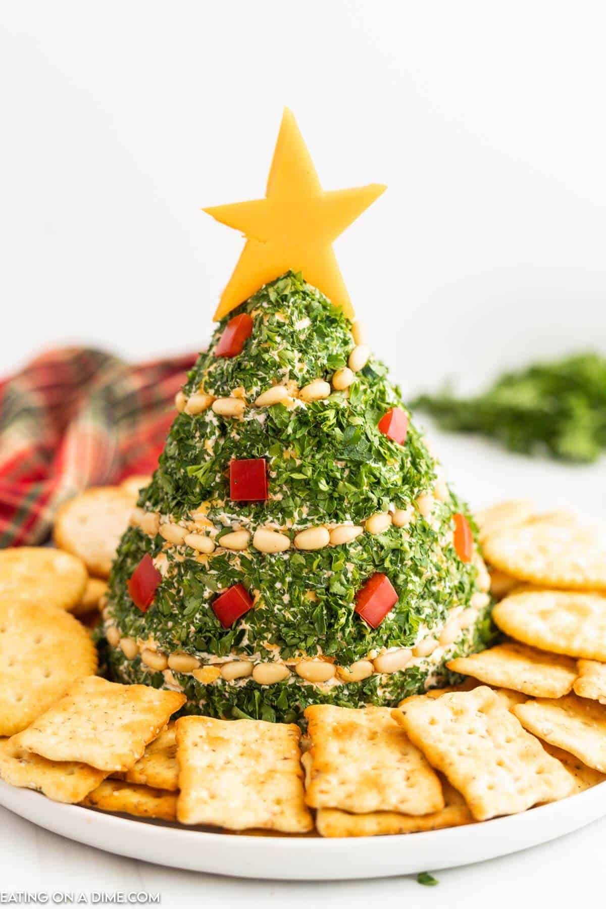 Christmas Tree Cheese Ball decorated with parsley, pine nuts, and red peppers, served with crackers β a fun and festive option for holiday appetizers and unique cheese ball recipes.