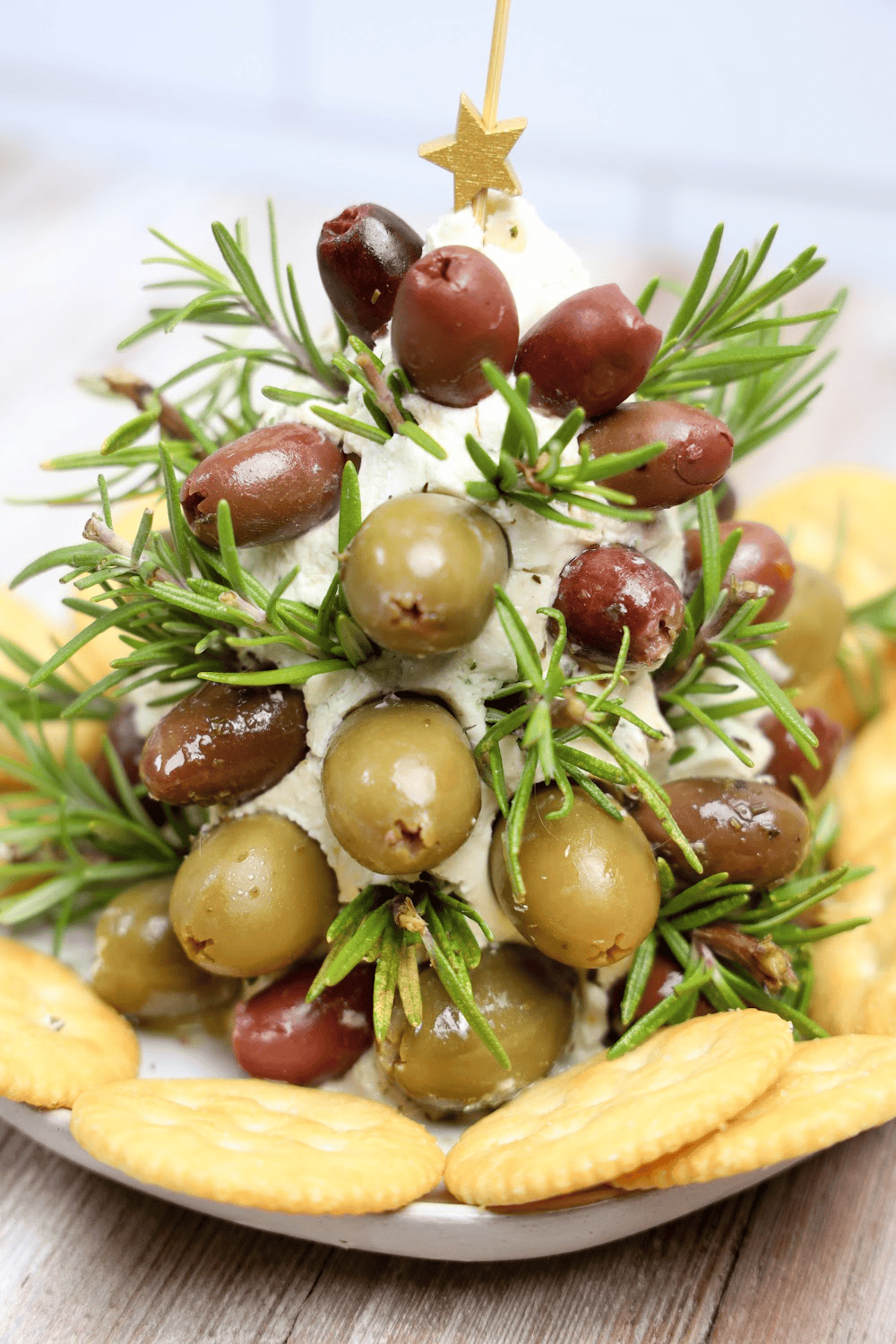 Christmas Tree Cheese Ball topped with green and black olives and sprigs of rosemary, served with crackers a festive favorite for holiday appetizers and unique cheese ball recipes.