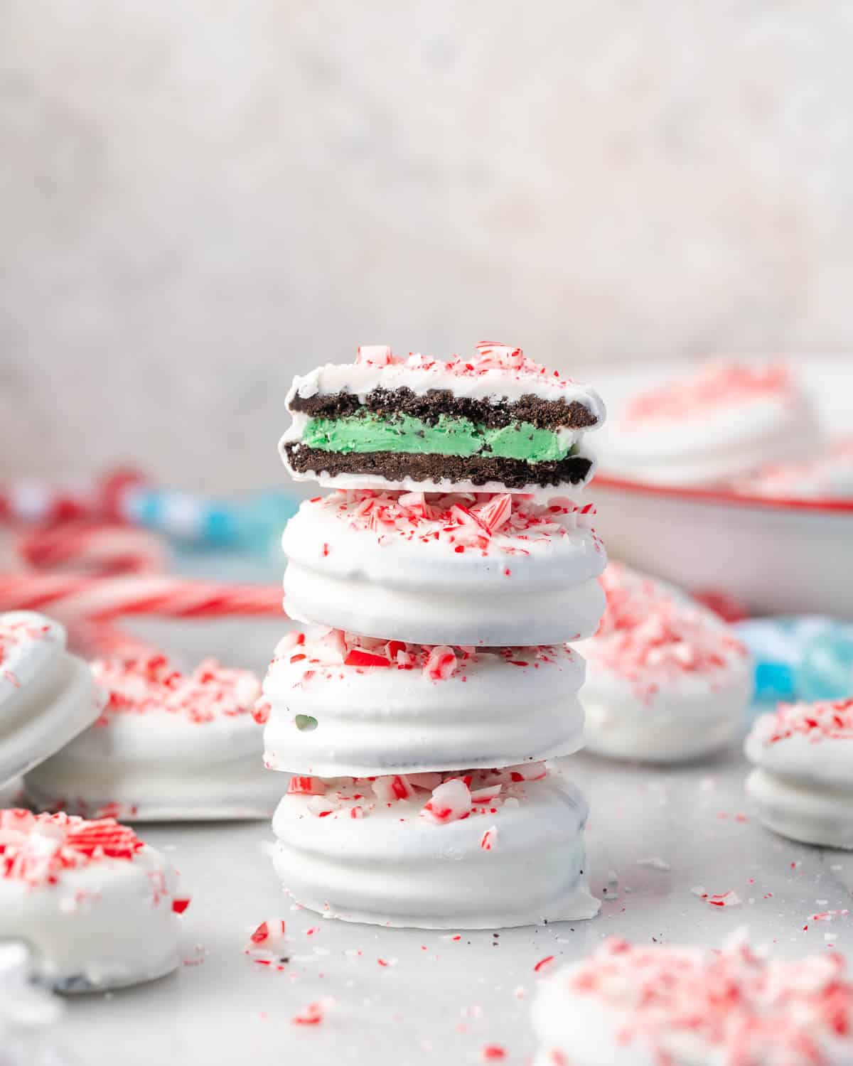Stacked peppermint bark Oreos coated in white chocolate and topped with crushed candy canes, with one cookie bitten to reveal a green peppermint filling.