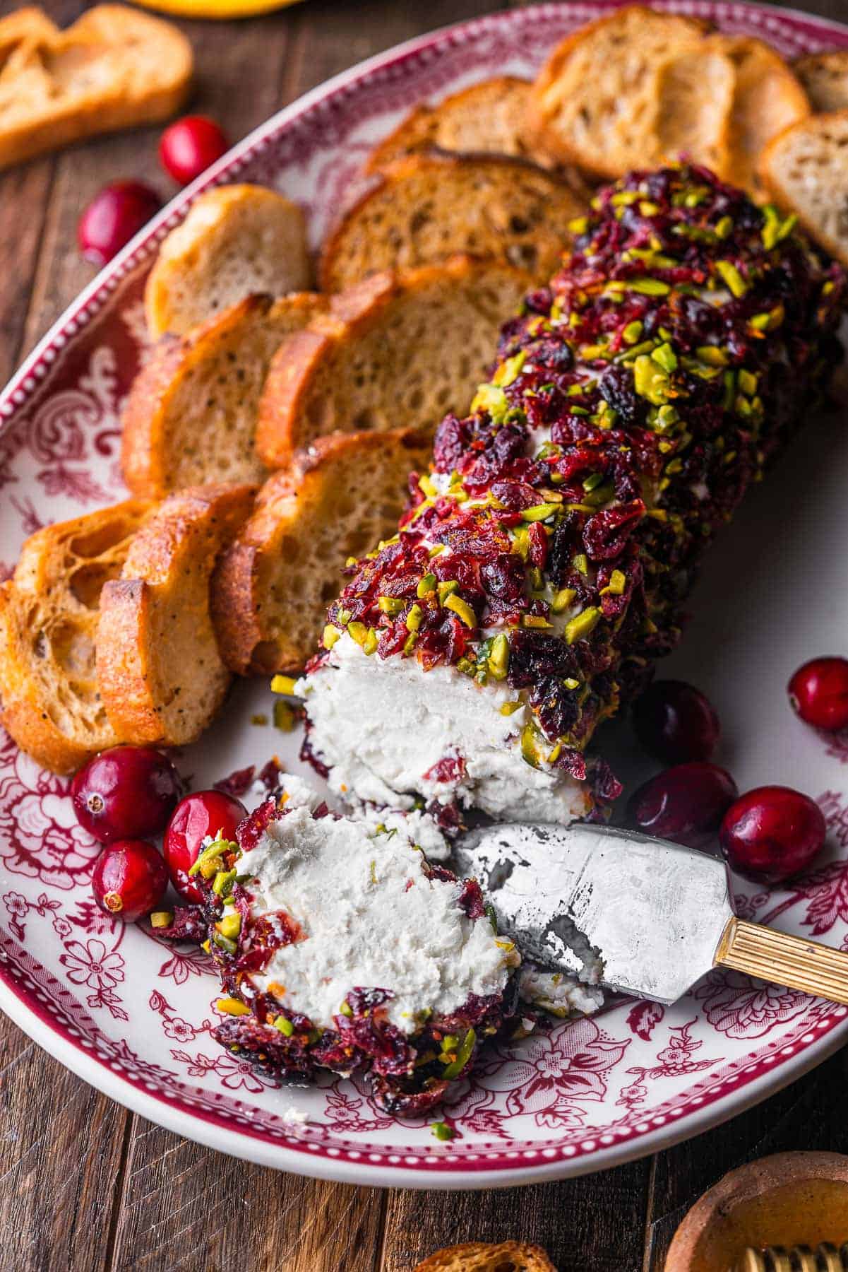Cranberry Pistachio Goat Cheese Log on a holiday platter surrounded by toasted crostini a beautiful and simple choice for cheese ball recipes easy and festive appetizers easy finger food.