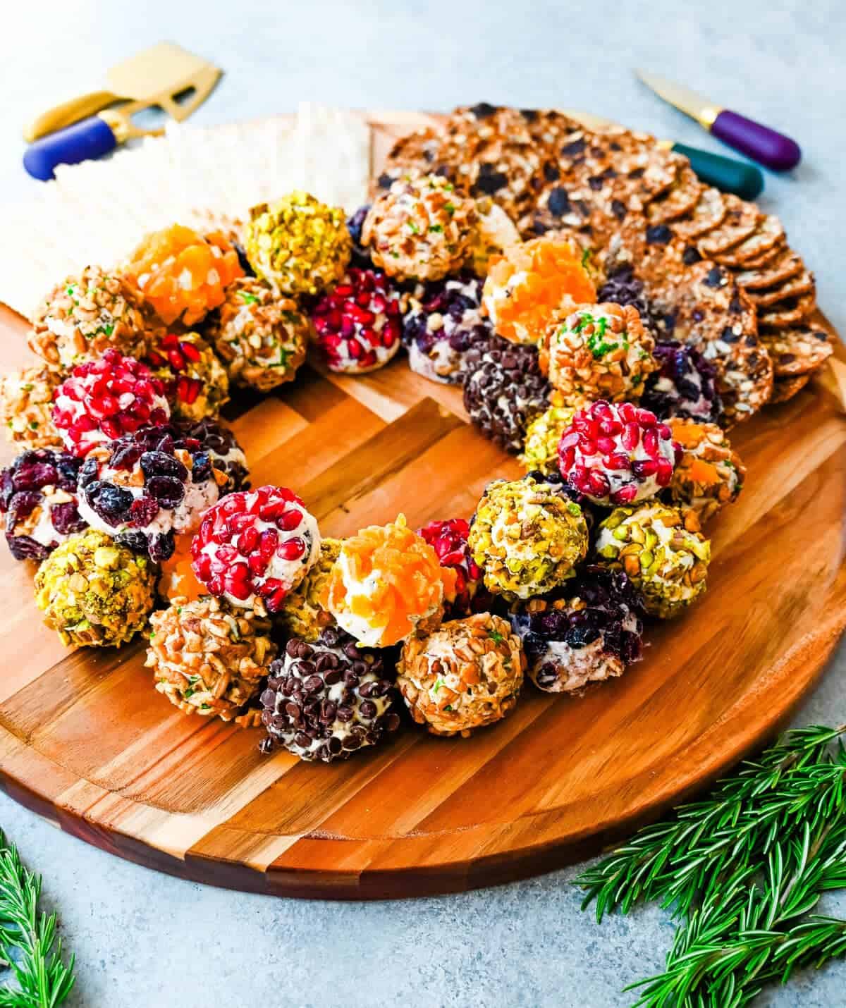 Mini cheese balls arranged in a festive holiday wreath shape, coated in toppings like pomegranate, pistachios, herbs, and dried fruit perfect for holiday cheese ball appetizers.