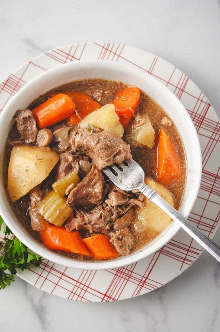 Bowl of slow cooker beef stew with tender beef, carrots, potatoes, celery, and mushrooms in a rich beef broth, served in a white bowl—classic crockpot beef stew made with hearty vegetables and deep flavor.