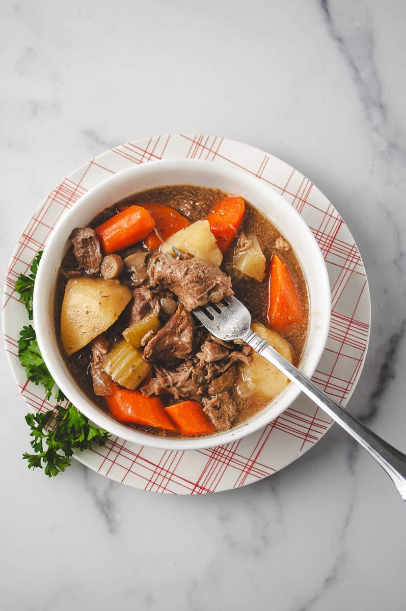 Top-down view of crockpot beef stew with tender beef, carrots, potatoes, mushrooms, and celery in a rich, savory broth—easy slow cooker recipe perfect for a hearty family meal.