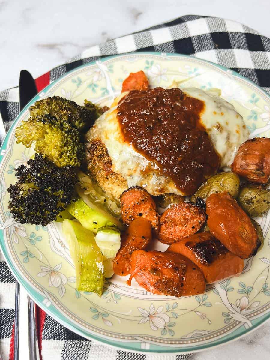 Plate of sheet pan chicken parmesan with parmesan crusted chicken, melted mozzarella, marinara sauce, and roasted vegetables served as a one pan meal.