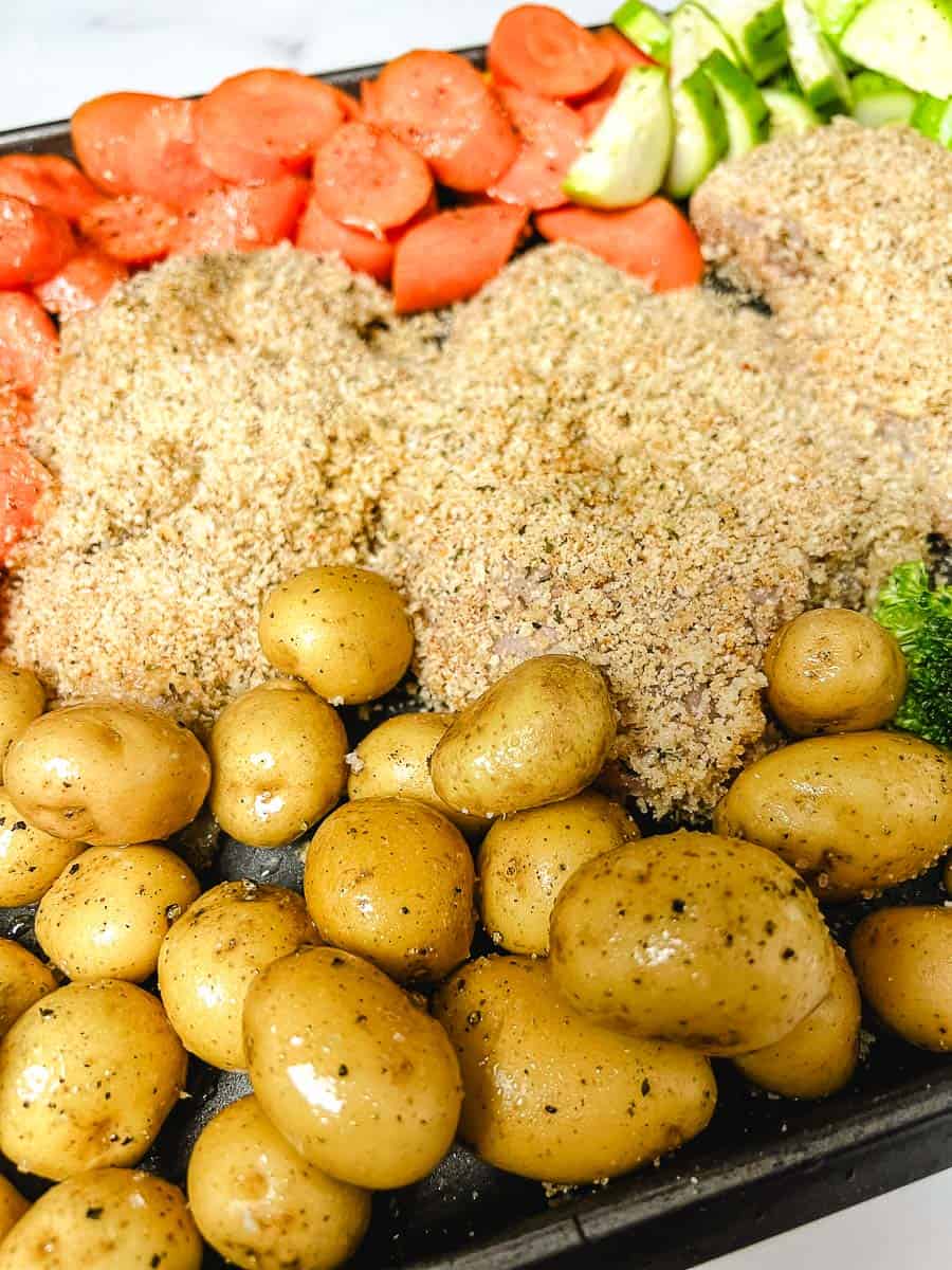 Breaded chicken and vegetables arranged on a sheet pan before baking, ready for a simple one pan chicken dinner chicken before it is cooked.