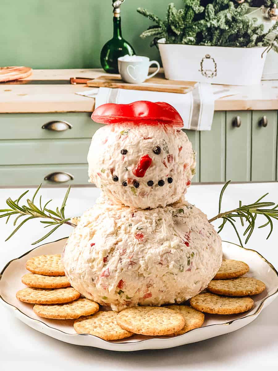 Snowman holiday cheese ball made with cream cheese and white cheddar, decorated with red pepper and chives, served with crackers as an easy holiday appetizer and festive cheese ball recipe for parties.