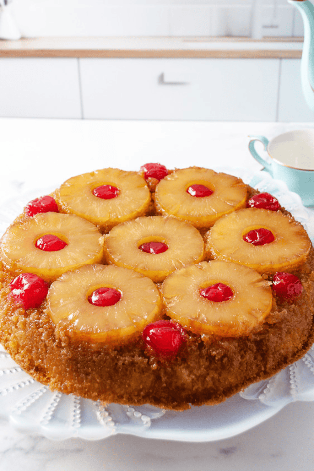 Pineapple upside down cake classic skillet recipe on a white cake stand topped with caramelized pineapple rings and bright red maraschino cherries. 