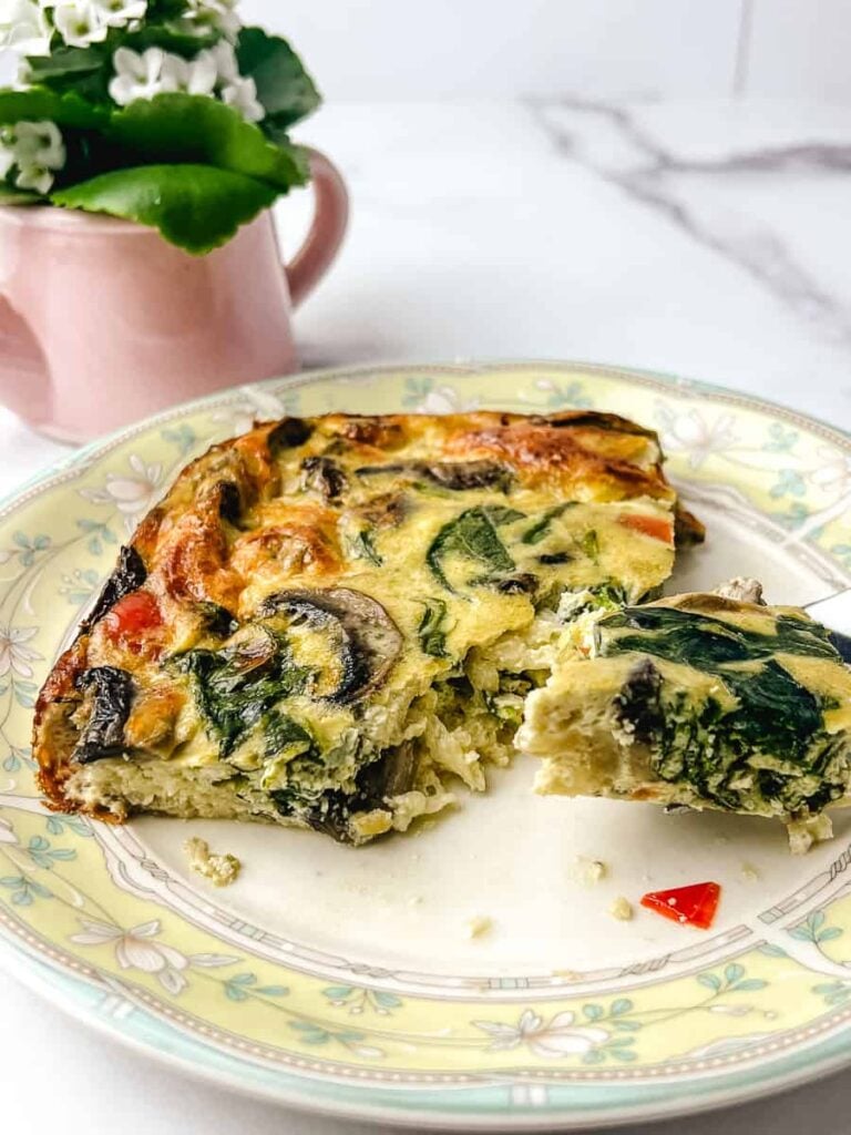 Slice of mushroom spinach egg casserole on a plate, showing layers of eggs, sautéed mushrooms, spinach, and melted cheese for an easy healthy breakfast