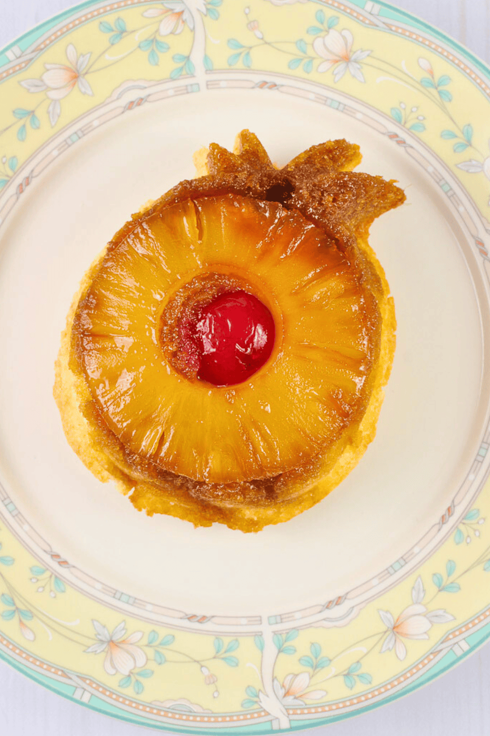 Pina colada ambrosia salad served in a glass sundae dish topped with mini marshmallows shredded coconut and pecans on a rustic wood background. 