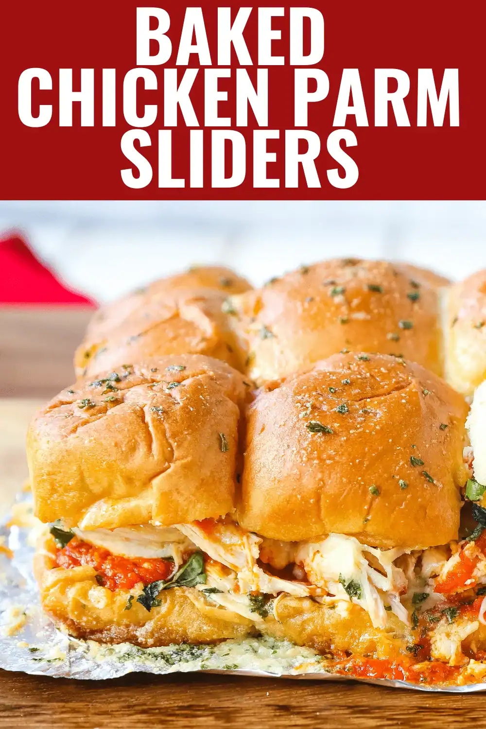Baked chicken parmesan sliders with marinara sauce and melted mozzarella cheese oozing out of golden garlic herb rolls on a foil lined pan, easy hot graduation party slider recipes for a crowd