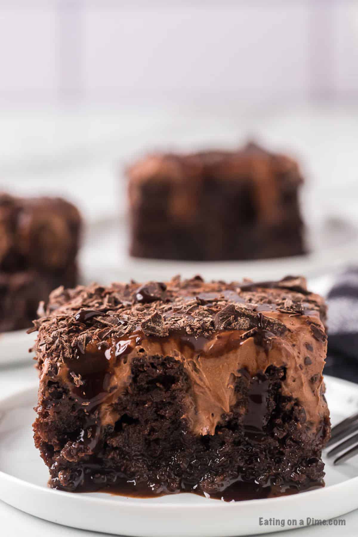 A thick slice of chocolate poke cake with creamy chocolate mousse frosting and chocolate shavings on top, with fudgy chocolate sauce soaking into every layer.