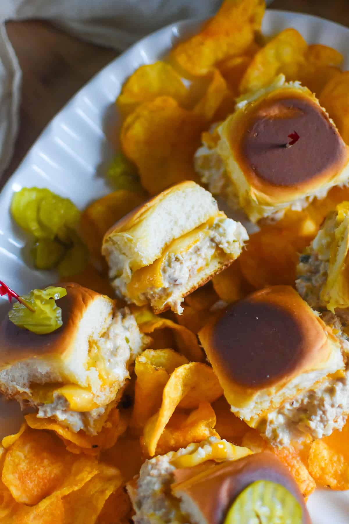 Baked tuna melt sliders with melted cheddar cheese on soft rolls served on a white plate with chips and pickle slices, easy graduation party slider ideas for a crowd
