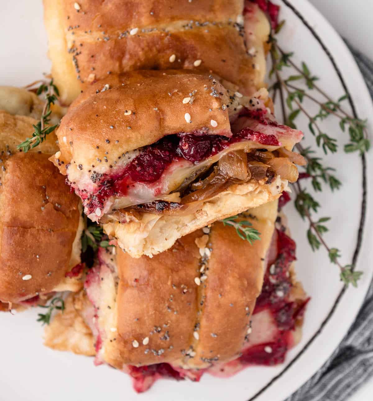 Turkey and cranberry sliders with caramelized onions and melty havarti cheese on soft rolls on a serving board, elegant graduation party slider ideas for a crowd
