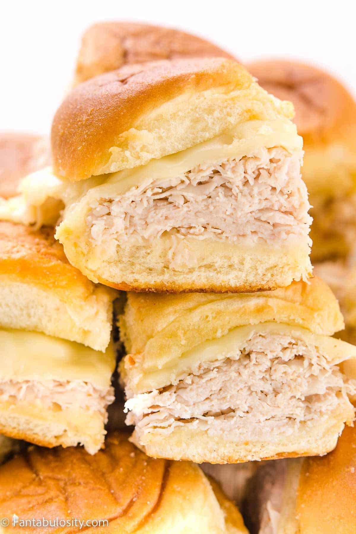 Turkey and cheese sliders stacked and cut in half showing layers of shredded turkey and melted Swiss cheese on soft golden rolls on a white background, easy make-ahead graduation party sliders for a crowd