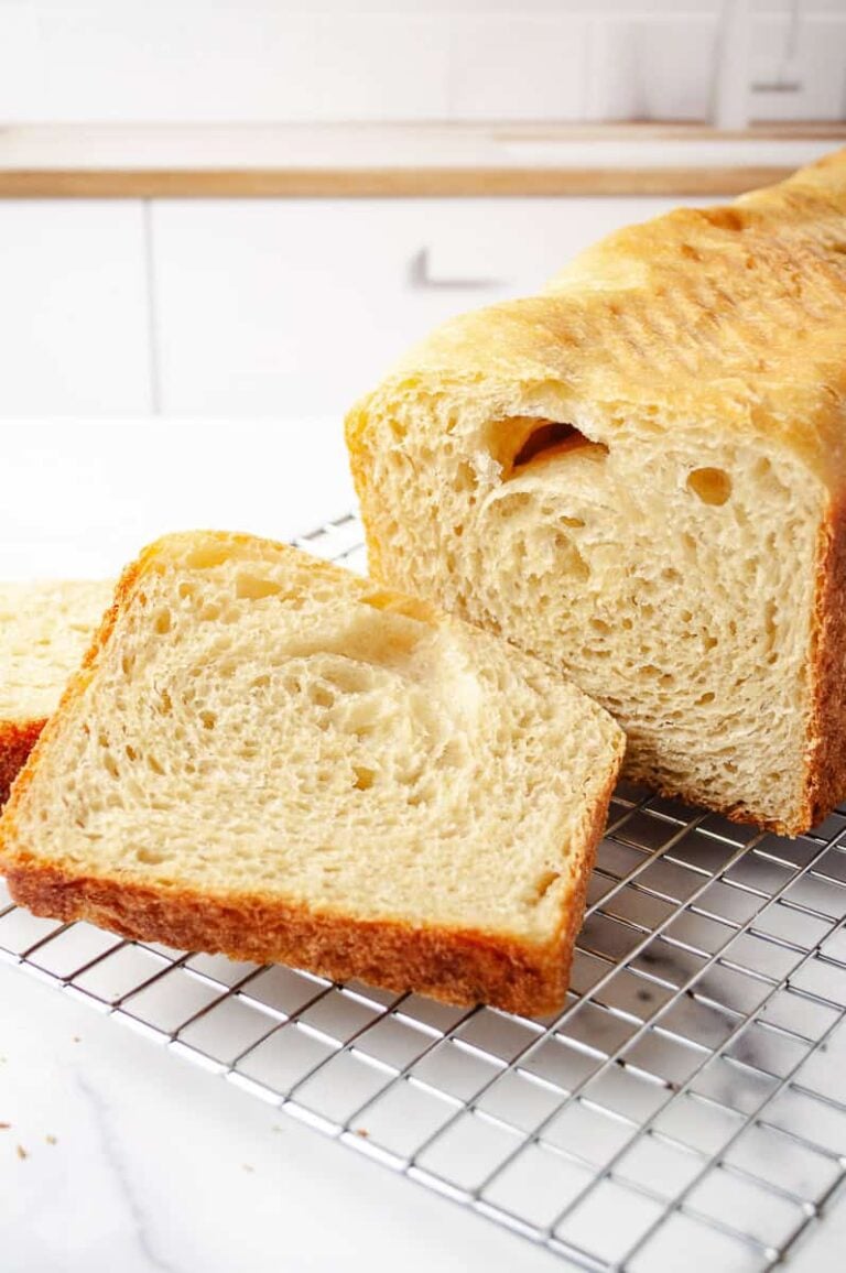 sourdough bread sandwich loaf on a cooling rack two cut slices and one slice with soft pillow texture in a white kitchen on a white counter.